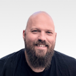 Head-and-shoulders portrait of a smiling bald man with a full beard in a black shirt.