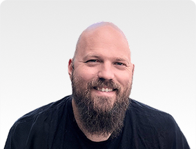 Head-and-shoulders portrait of a smiling bald man with a full beard in a black shirt.