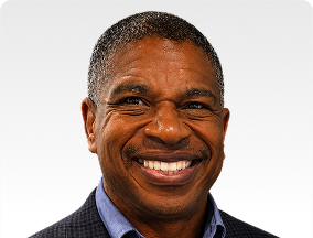 Smiling man wearing a dark blazer and light blue shirt, facing the camera.