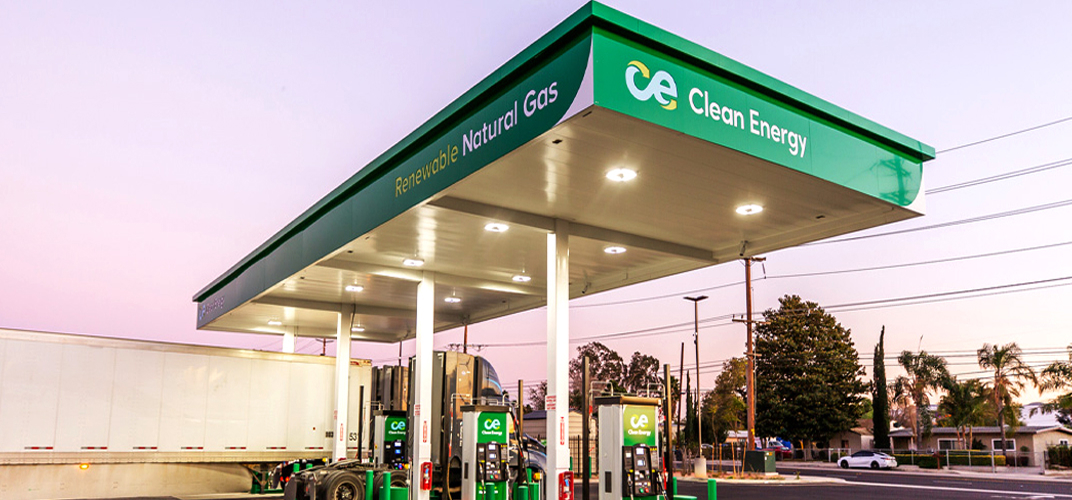Gas fueling station canopies with Clean Energy branding and Renewable Natural Gas signage at dusk, pumps in foreground and a semi-trailer nearby.